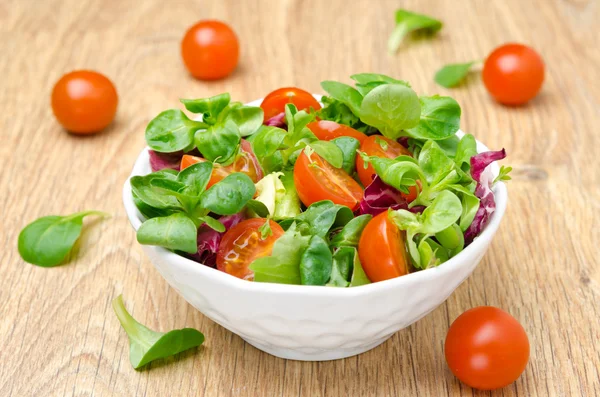 Ensalada fresca y tomates cherry en un tazón sobre fondo de madera —  Fotos de Stock