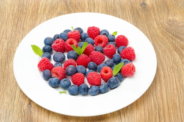 新鲜树莓和蓝莓的木桌上盘子上 — 图库照片