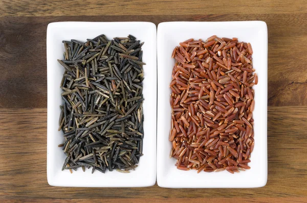 Red and wild rice in white the bowls on wooden background — Stock Photo, Image