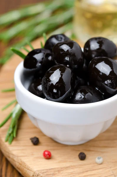 Zwarte olijven en specerijen op een houten bord, close-up verticaal — Stockfoto