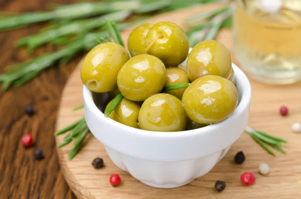 Groene olijven en specerijen op een houten bord — Stockfoto