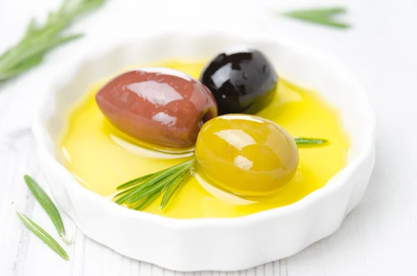 Tre sorters oliver och rosmarin i en skål med olivolja — Stockfoto