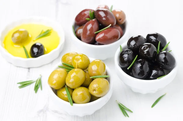 Tres tipos de aceitunas en cuencos, romero fresco y aceite de oliva — Foto de Stock