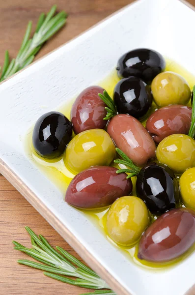 White wooden bowl with a variety of olives and rosemary in oil — Stock Photo, Image