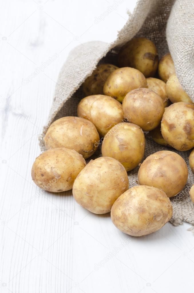 new potatoes in a sack on a white wooden board