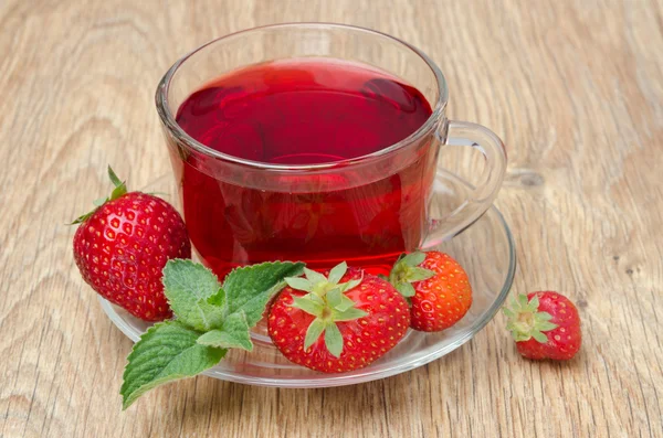 Tazza di tè rosso con fragole e menta su uno sfondo di legno — Foto Stock