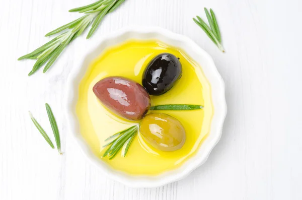 Three kinds of olives and rosemary in a bowl with olive oil — Stock Photo, Image