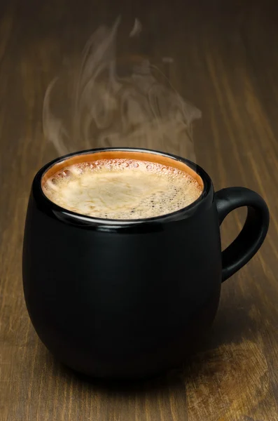 Black mug of coffee with foam on a wooden table — Stock Photo, Image