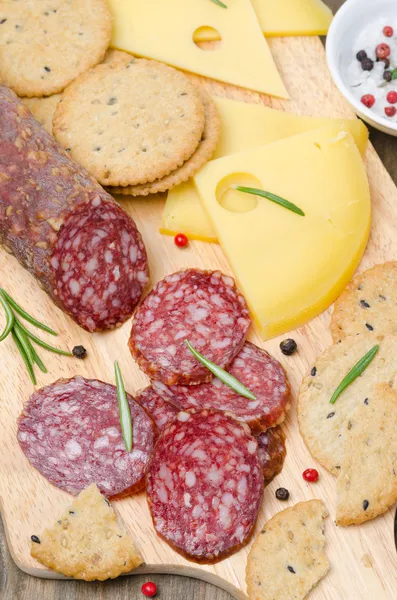 Salami italiano, queso y galletas saladas en una tabla de cortar — Foto de Stock
