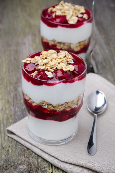 Dois copos com sobremesa em camadas com iogurte, granola e cereja — Fotografia de Stock