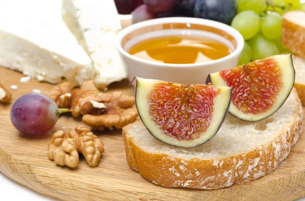 Cheese, bread, figs, grapes, honey and nuts on a wooden board — Stock Photo, Image