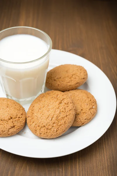Vaso de leche y galletas de avena en un plato, primer plano —  Fotos de Stock