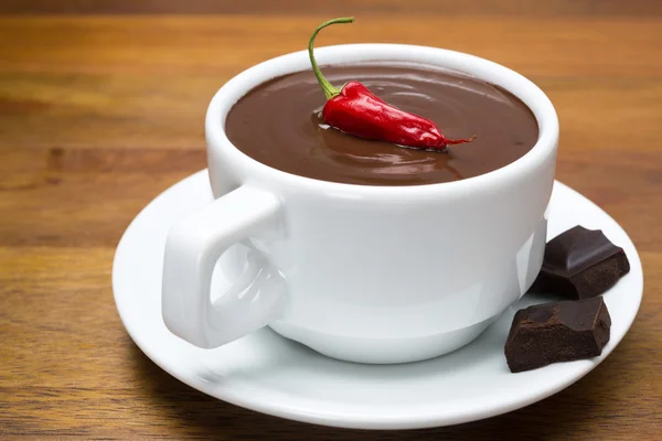 Cup of hot chocolate with chili peppers on a wooden background — Stock Photo, Image