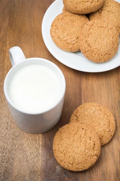 Biscoitos de aveia e uma caneca de leite em uma tábua de madeira — Fotografia de Stock