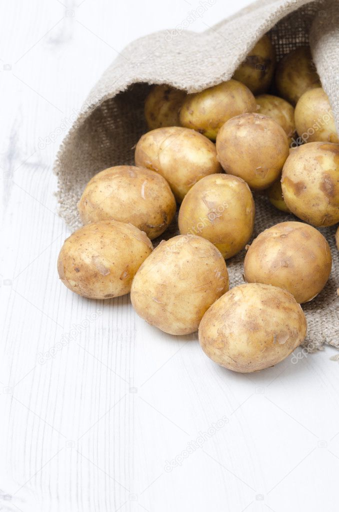 new potatoes in a sack on a white wooden board, vertical