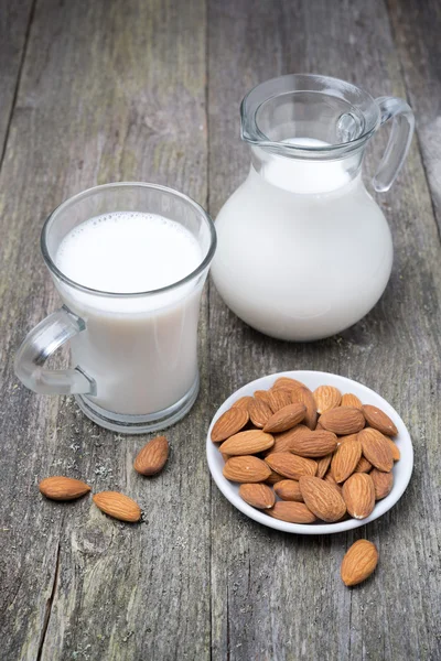 Krug und Glasbecher mit Mandelmilch auf einem Holztisch — Stockfoto