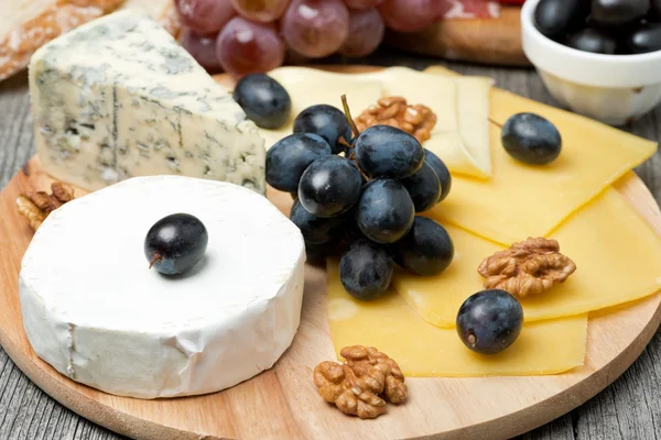 Assorted cheese and grapes on a wooden board — Stock Photo, Image