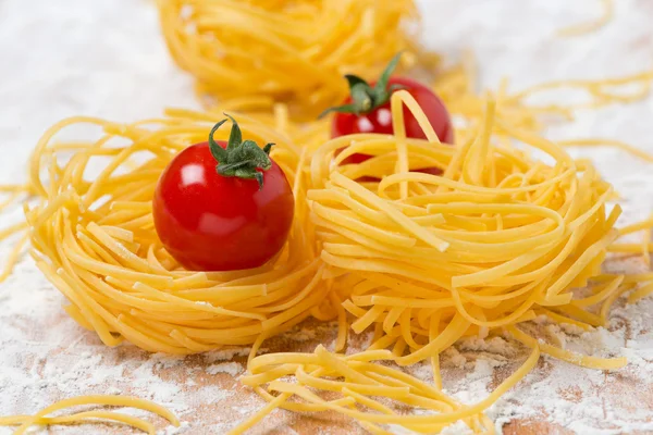 Nido italiano de pasta de huevo, tomates cherry en una tabla de cortar — Foto de Stock