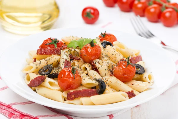 Паста с колбасой, помидорами черри и оливками на тарелке — стоковое фото