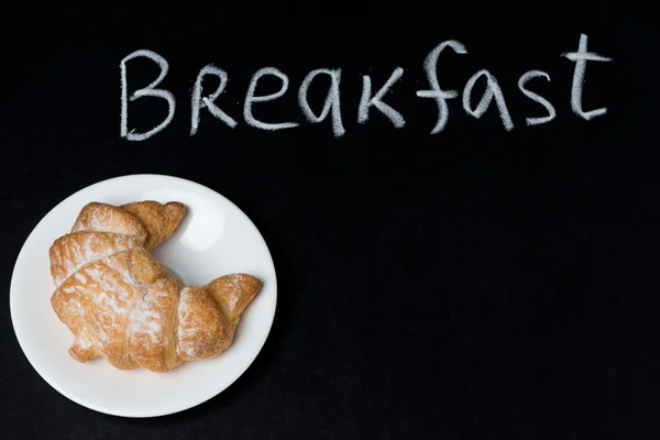 Croissant sur une assiette au tableau noir et le mot petit déjeuner — Photo
