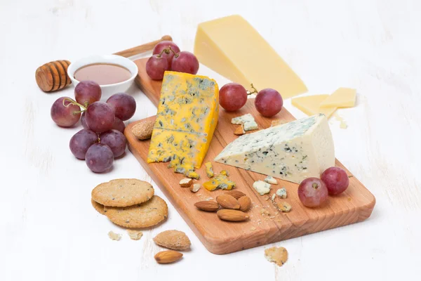 Rozmanité sýry, hrozny, ořechy a sušenky na dřevěném prkénku — Stock fotografie