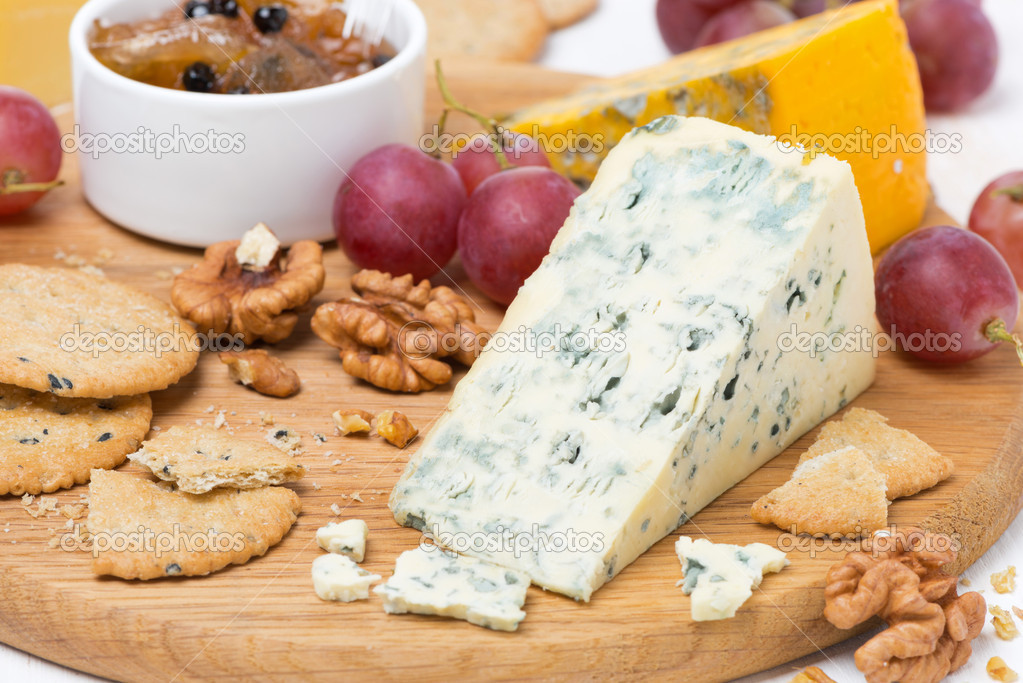 cheeses with mold, grapes, crackers, jam and nuts on a board