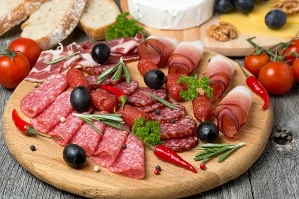 Assorted meats and sausages, olives and spices on a wooden board — Stock Photo, Image