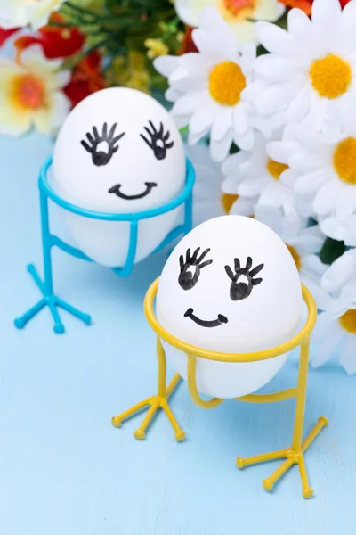 Dos divertidos huevos sonrientes en soportes y flores para Pascua —  Fotos de Stock