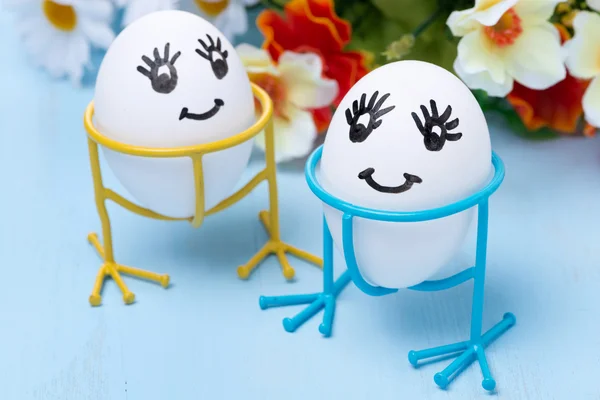 Dos huevos sonrientes divertidos en soportes y flores, enfoque selectivo —  Fotos de Stock