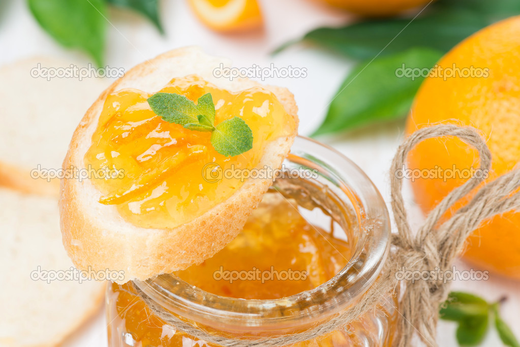 orange jam in a glass jar and piece of baguette