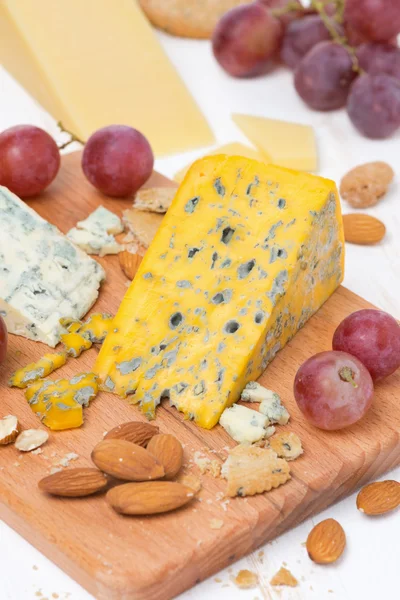 Assorted cheeses, grapes and nuts on a wooden cutting board — Stock Photo, Image