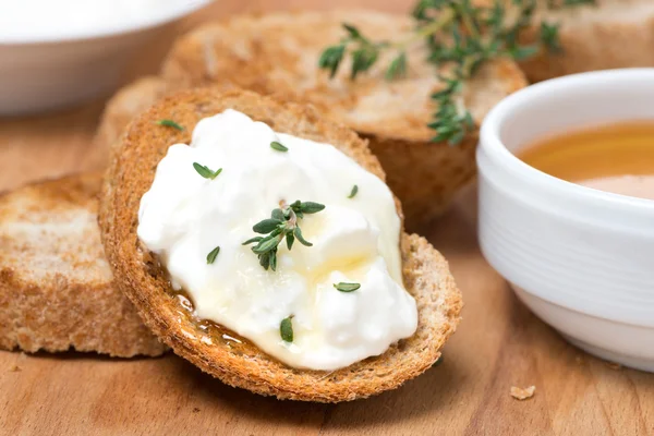 Toasts with goat cheese, honey and thyme on wooden board — Stock Photo, Image