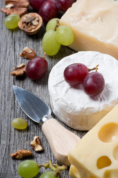 Assortment of cheeses, grapes and walnuts on a wooden background — Stock Photo, Image