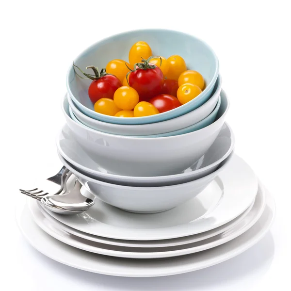 Bowls, plates, cutlery and cherry tomatoes, isolated — Stock Photo, Image