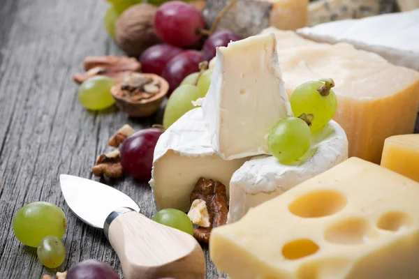 Cheeses, grapes and walnuts on a wooden background — Stock Photo, Image