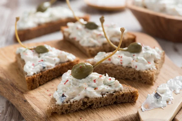 Toasts with cheese pate and capers on a wooden board — Stock Photo, Image