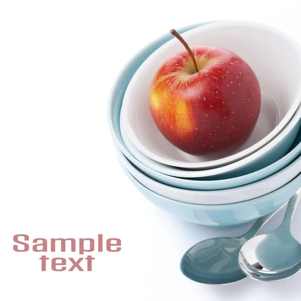 Diferentes cuenco limpio, cucharas y manzana roja, aislado —  Fotos de Stock