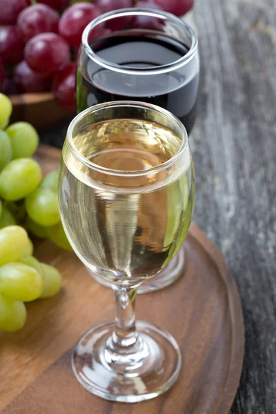 Copo de vinho branco e tinto, uvas frescas em uma tábua de madeira — Fotografia de Stock