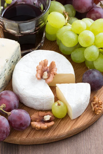 Assorted soft cheeses and fresh grapes on a wooden board — Stock Photo, Image