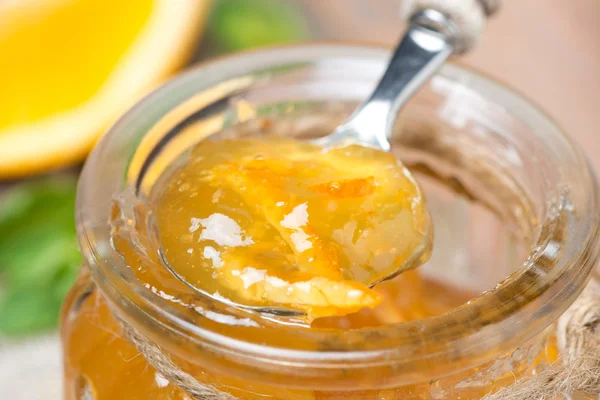Spoon of orange marmalade in a glass jar, close-up — Stock Photo, Image