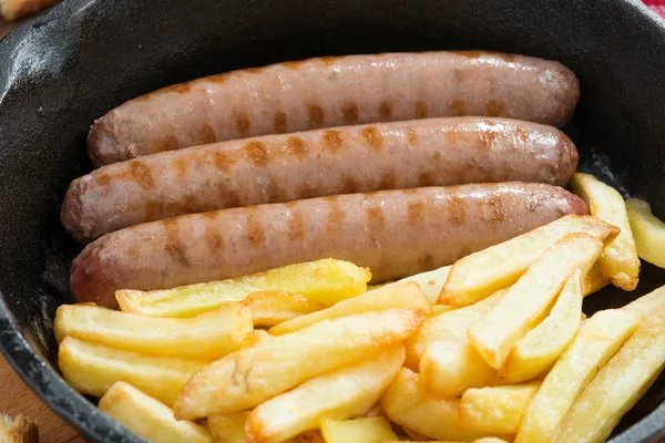 Grilled sausages with French fries in a frying pan, close-up — Stock Photo, Image