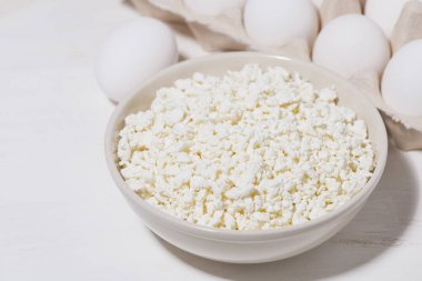 Bir kase taze çiftlik peyniri ve yumurta beyaz arka planda, yatay yakın plan