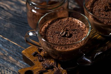 Tahta arka planda cam bardaklarda çikolatalı krema, yatay üstte.