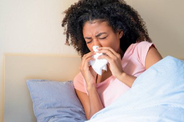 Yatakta hasta hisseden ve burnunu silen siyah bir kadın.