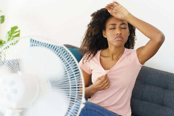 African woman suffering from heat in front of fan at home