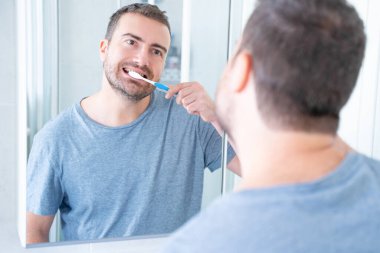 Bir adam sabah diş fırçası kullanarak ağız temizliği yapıyor.