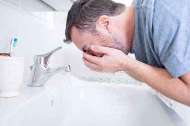 Adam sabah uyanmak için yüzünü temizliyor.