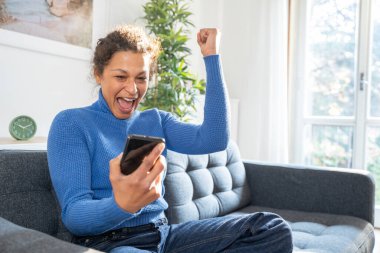 Black woman celebrates getting good news on mobile phone