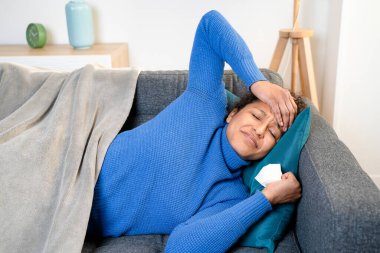 Black woman suffering head pain at home on the sofa