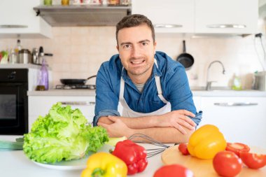 Evdeki mutfakta bir adam fotoğraf makinesinin portresine bakıyor.
